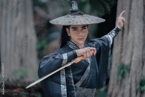 Chinese warriors wearing old traditional costumes. An elegant warrior in a conventional black robe holding a sword wearing a woven bamboo hat in the forest. Ancient Chinese warrior portrait.