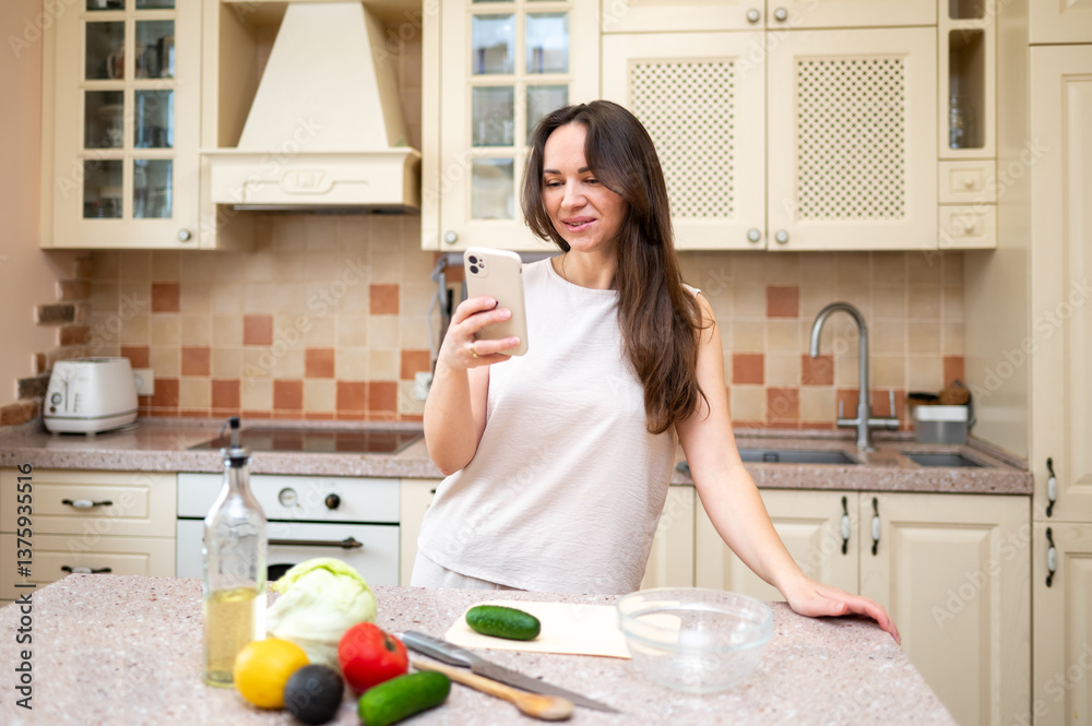Smiling woman using smartphone while preparing fresh vegetable salad in cozy kitchen. Healthy lifestyle, home cooking and online recipe inspiration Smiling woman using smartphone while preparing fresh vegetable salad in cozy kitchen. Healthy lifestyle, home cooking and online recipe inspiration