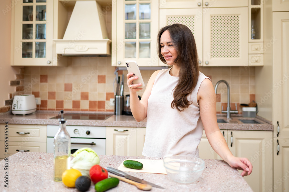Smiling woman using smartphone while preparing fresh vegetable salad in cozy kitchen. Healthy lifestyle, home cooking and online recipe inspiration Smiling woman using smartphone while preparing fresh vegetable salad in cozy kitchen. Healthy lifestyle, home cooking and online recipe inspiration