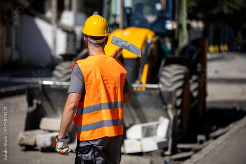 Construction worker prepares for roadwork during the day with heavy machinery in the background