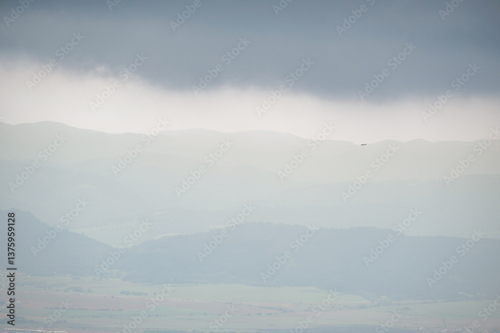 Foggy mountain view from the far with low dark clouds and a silhouette of an airplane on the edge of the mountains, Slovakia Foggy mountain view from the far with low dark clouds and a silhouette of an airplane on the edge of the mountains, Slovakia