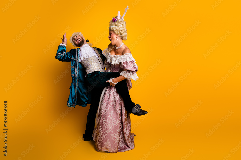 Fototapeta premium Playful couple dressed in vintage costumes posing against a bright yellow background, evoking a mix of historical elegance