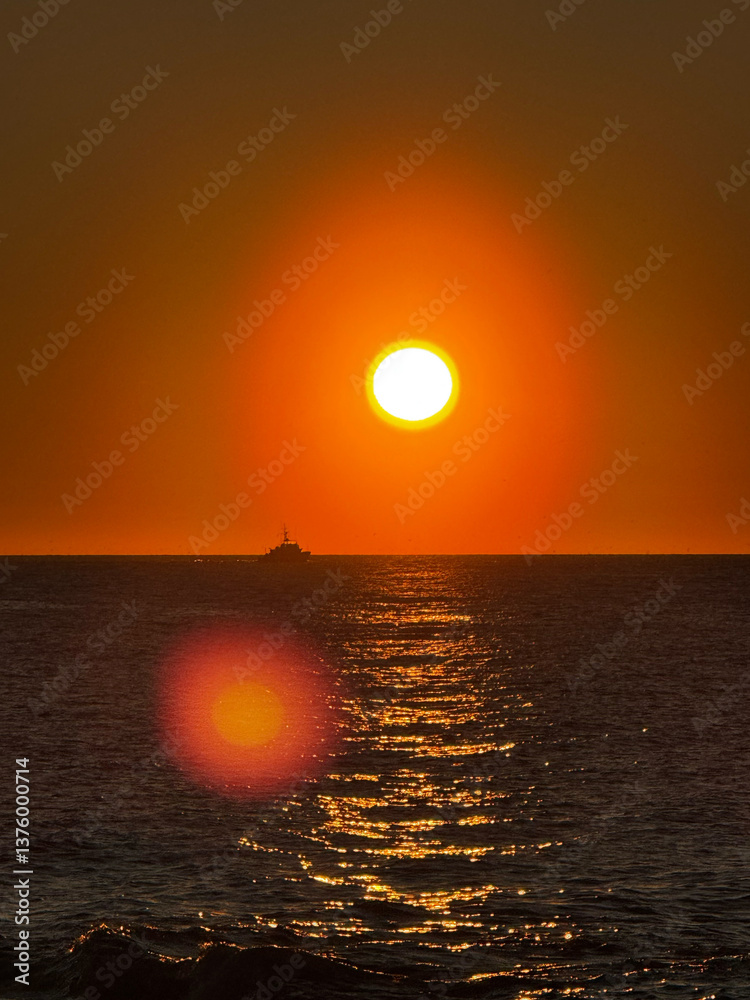 Sunset over ocean with boat and golden sun reflection