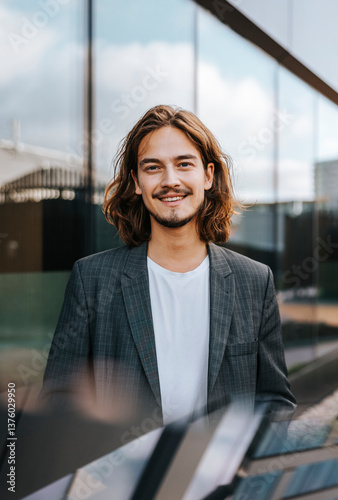 Portrait of smiling young male entrepreneur with long hairs outside office building