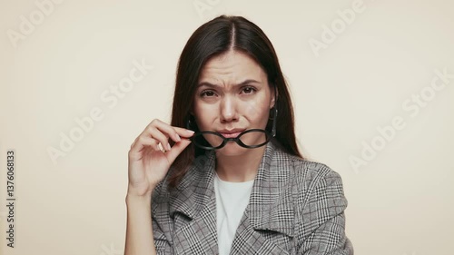 A confident young woman in a stylish suit removes her glasses with an arrogant expression, scrutinizing the situation.