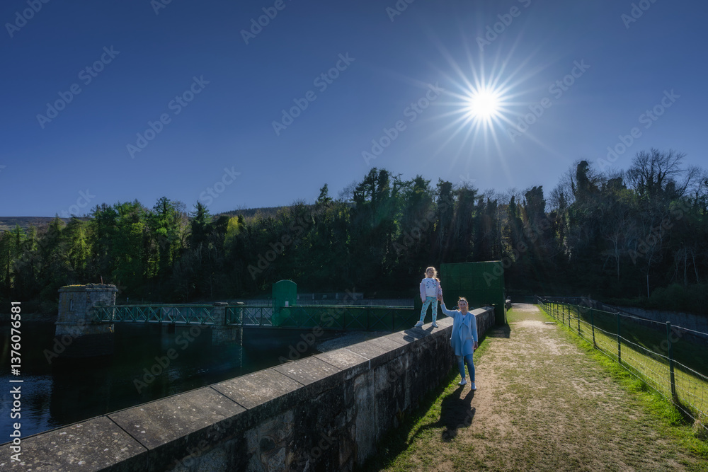 On a bright and sunny day, mother and daughter set out to explore a picturesque reservoir, surrounded by vibrant greenery, tall trees, and a clear blue sky, Bohernabreena Reservoir, Dublin, Ireland