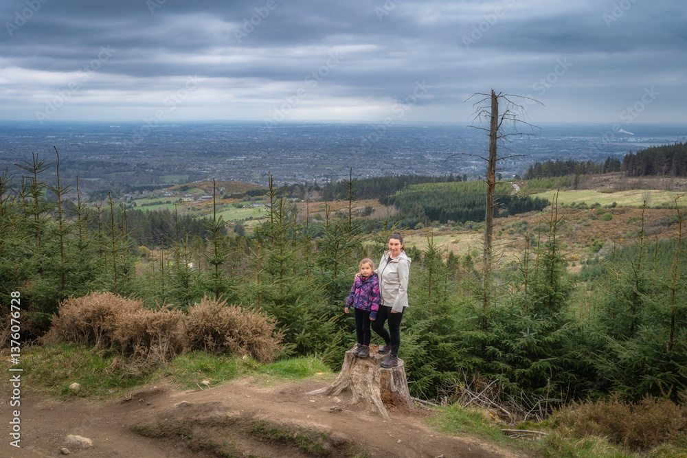 A loving mother and her child stand proudly on a majestic tree stump at a scenic overlook, surrounded by vibrant greenery and breathtaking landscapes, Wicklow, Dublin, Ireland