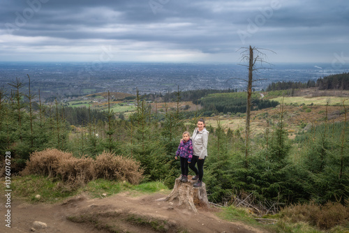 Obraz na płótnie A loving mother and her child stand proudly on a majestic tree stump at a scenic overlook, surrounded by vibrant greenery and breathtaking landscapes, Wicklow, Dublin, Ireland w salonie