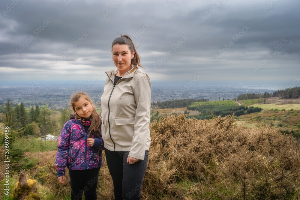 A mother and daughter happily pose together on a picturesque hillside, surrounded by a stunning and colorful scenic view in the background, creating a memorable moment, Wicklow, Dublin, Ireland