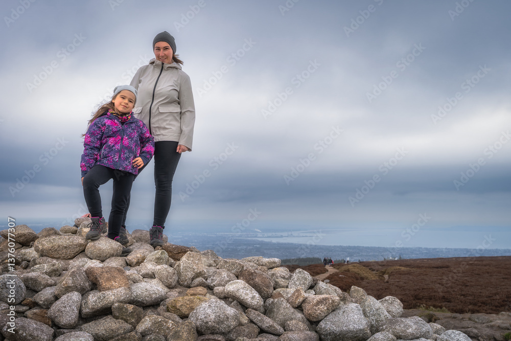 A mother and her daughter are joyfully posing atop a rocky mound, showcasing their delightful adventure in nature against a beautifully moody sky backdrop, Wicklow, Dublin, Ireland