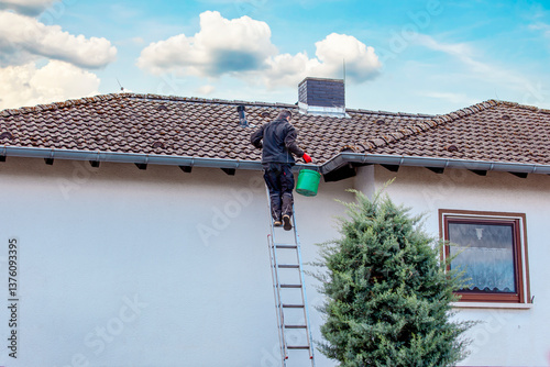 worker on the roof. man on ladder cleaning house gutter from leaves and dirt. 
