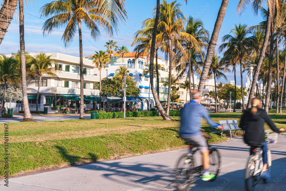 A vibrant street scene in Miami Beach with palm trees, colorful Art Deco-style buildings, and motion blurred cyclists along a sunny beachfront promenade
