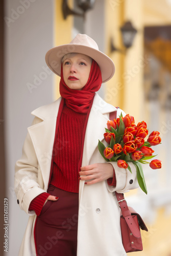 Young beautiful girl in early spring with tulips on the city street.