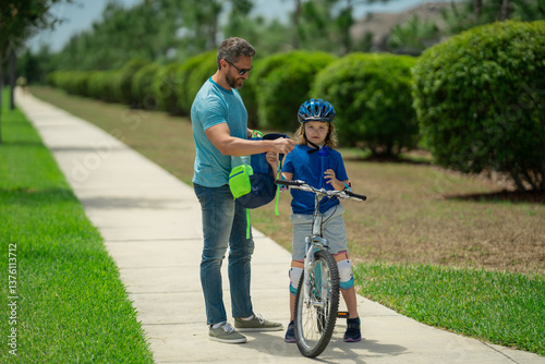 Happy family. Father and son riding bike in park. Child in safety helmet with father riding bike in summer day. Father teaching son riding bike. Fatherhood. Support parent. Fathers day. Child care.