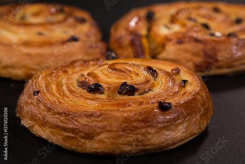 Puff pastry snail with maple syrup and raisins on a black background, top view