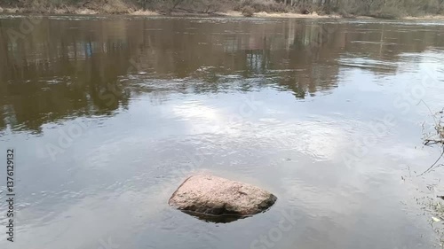 A solitary boulder partially submerged in calm water, showcasing natural rock formations and the beauty of a serene aquatic landscape. 