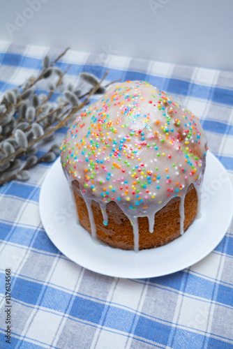 Tree tasty decorate Easter cakes lie on a round white wooden plate on a white wooden table. A tray with cakes and flowers stand on the table.