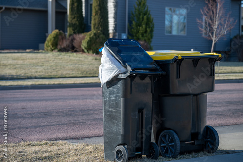 Overfilled garbage bin on the street curb of a residential area on trash pickup day.
