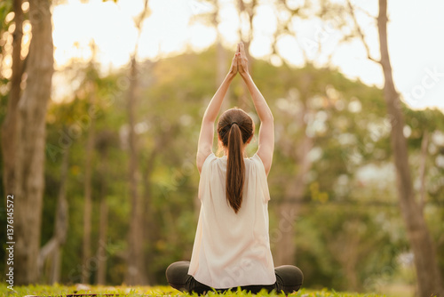 Fotografija Young Asian woman practicing yoga in a quiet park, gracefully in a relaxed pose, relaxing and strengthening her body, flexibility and relaxation amidst the green grass