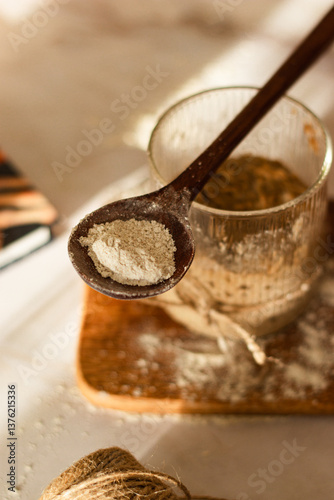 Active sourdough starter in a glass. Rye leaven for bread and kitchen wooden utensil on rustic background. Traditional bread baking concept. Close-up. Selective focus. Blurred background.