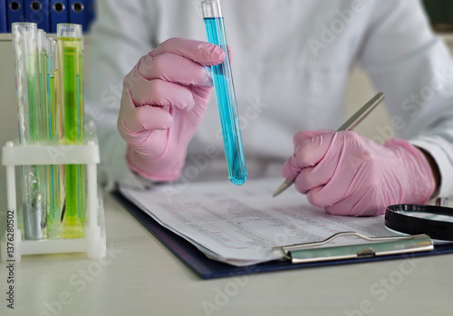 A scientist examines a blue liquid in a test tube in a lab. Lab technicians examine a test tube containing a sample of a blue poisonous toxic liquid concept