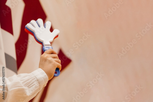 A fan's sports toy is a noisy hand with fingers in a woman's hand, red-white-blue on a beige background.