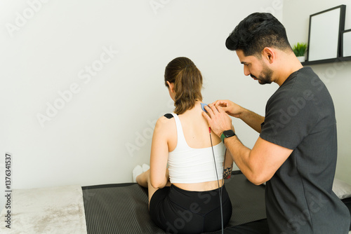 Картината върху платно Male physiotherapist applying electrode pads to female patient's back during tra