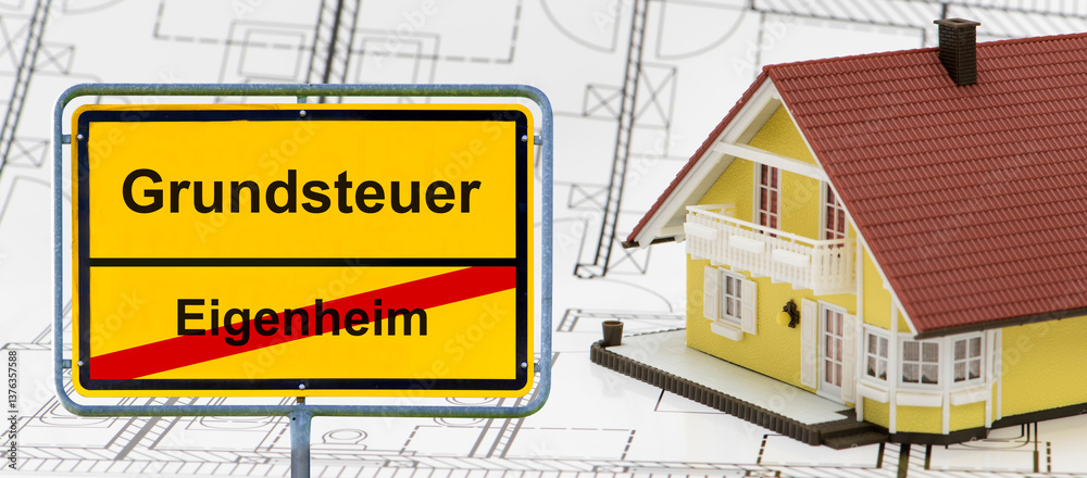 Ein Verkehrsschild ist beschriftet mit Eigenheim und Grundsteuer, vor einem Modellhaus als Eigenheim - FOTOMONTAGE