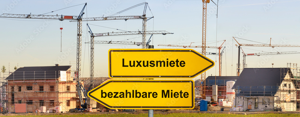 Ein Wegweiser ist beschriftet mit bezahlbare Miete und Luxusmiete vor einem Neubaugebiet für Wohnhäuser - FOTOMONTAGE