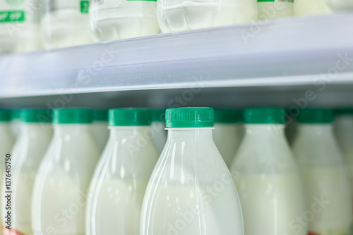 Bottles of milk with green caps arranged on a store shelf. Close-up view showcases uniformity and freshness of dairy packaging, emphasizing order and cleanliness in retail display.