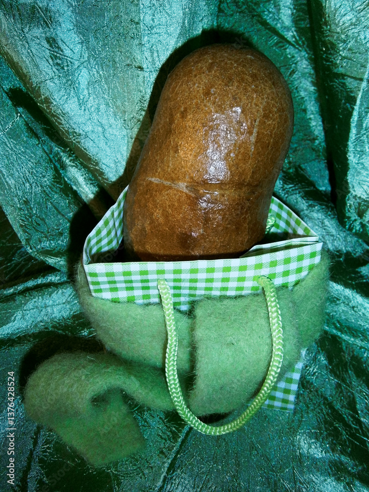 Ein gebackenes Brot zur Dekoration ein einem Beutel vor einem smaragdgrünen Vorhang