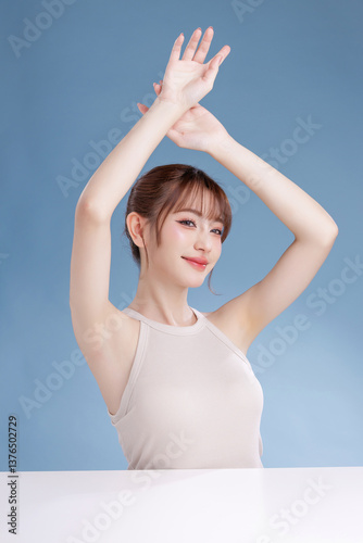 Beautiful young Asian woman model with bangs and natural makeup on face clean fresh skin show armpit on isolated blue background. Cute girl portrait, Facial treatment, Body care, Beauty and Spa.