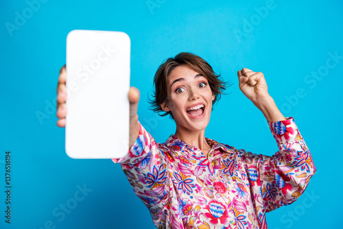 Obraz na płótnie Photo of nice delighted girl raise fist achieve arm hold show empty space smart phone screen isolated on blue color background w salonie