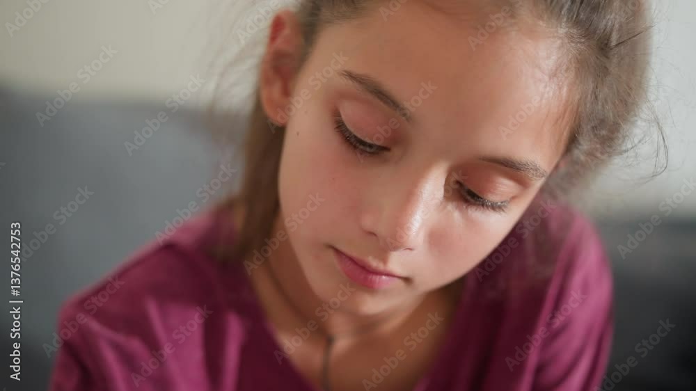 close up of cute girl in maroon top lost in thought with gentle expression as she gazes downward in quiet moment of focus and reflection on soft indoor background close up of cute girl in maroon top lost in thought with gentle expression as she gazes downward in quiet moment of focus and reflection on soft indoor background