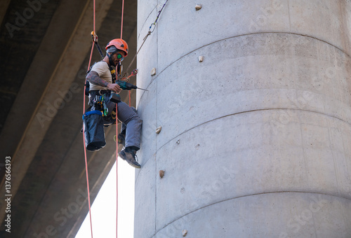 Rope access technician working on bridge concrete pillar using power drill