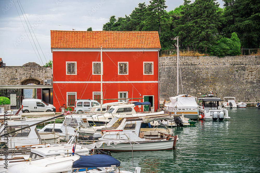 A picturesque Mediterranean harbor with colorful historic buildings, moored boats, and a tranquil waterfront, blending old-world charm with modern elements under a bright blue sky.