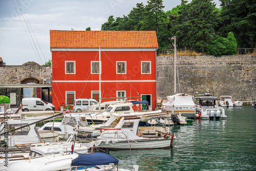 Obraz na płótnie A picturesque Mediterranean harbor with colorful historic buildings, moored boats, and a tranquil waterfront, blending old-world charm with modern elements under a bright blue sky. w salonie