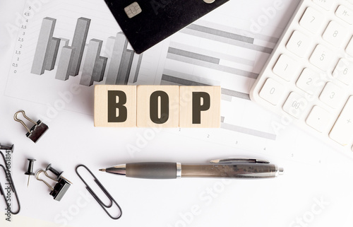Fotografie Wooden blocks spelling BOP on financial charts with calculator, pen, credit card