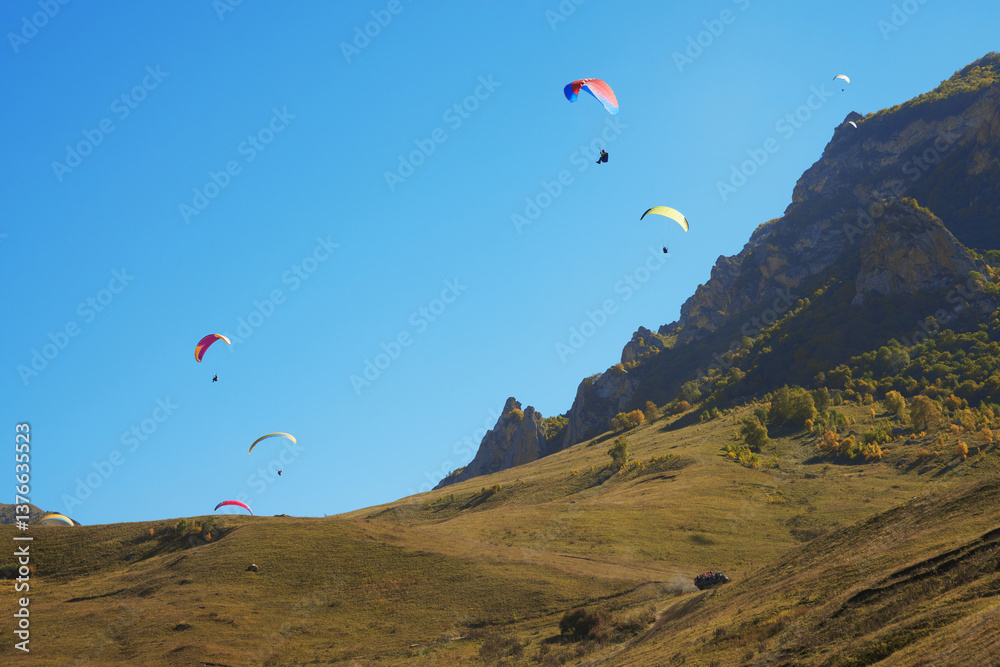 High-altitude paragliding. Many colorful paragliders in the sky on the picturesque background of a rocky mountain.