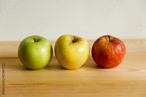 Three apples in a row: green, yellow and red. On a wooden table.