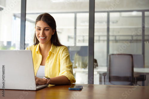 Smiling young indian business woman, it specialist using laptop at work in office. Female freelance entrepreneur working on online technological project on computer pc at company workplace. Copy space