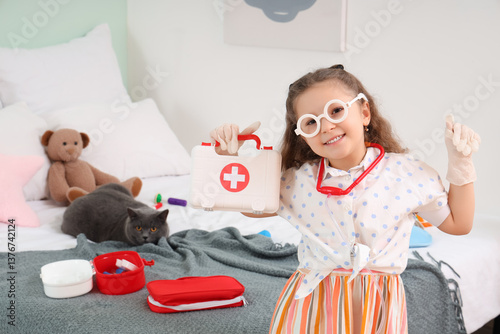 Cute little girl with first aid kit and British cat at home