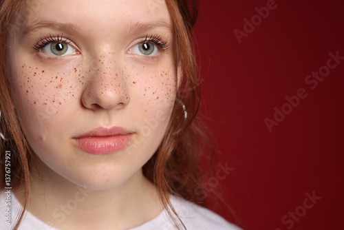 Beautiful teenage girl with freckles on red background, closeup. Space for text