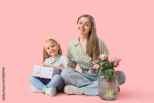Cute little girl greeting her mom for Mother's Day with gift box and tulips while sitting on pink background