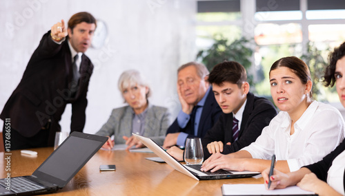 Angry male boss reprehending colleagues on meeting in modern office