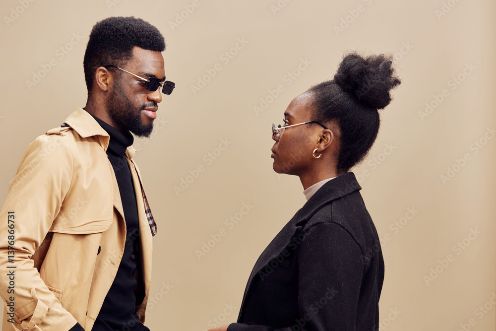 Stylish couple in sunglasses, wearing modern outfits, showcasing confidence and connection against a light brown background with a contemporary vibe