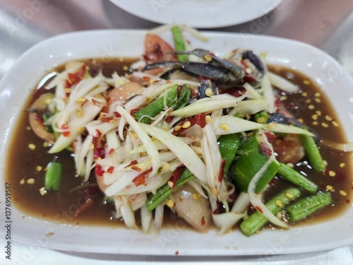 A plate of spicy Thai papaya salad (som tam) with salted crab, chili, and vegetables in a tangy, flavorful dressing.