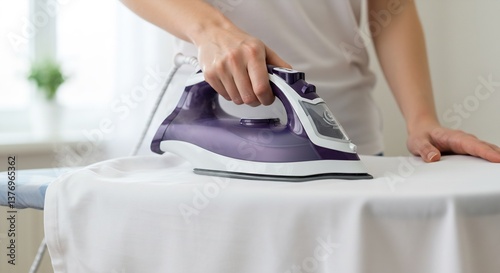 Close-up of a Woman's Hand Using a Modern Purple and White Steam Iron to Iron a White Cloth on an Ironing Board