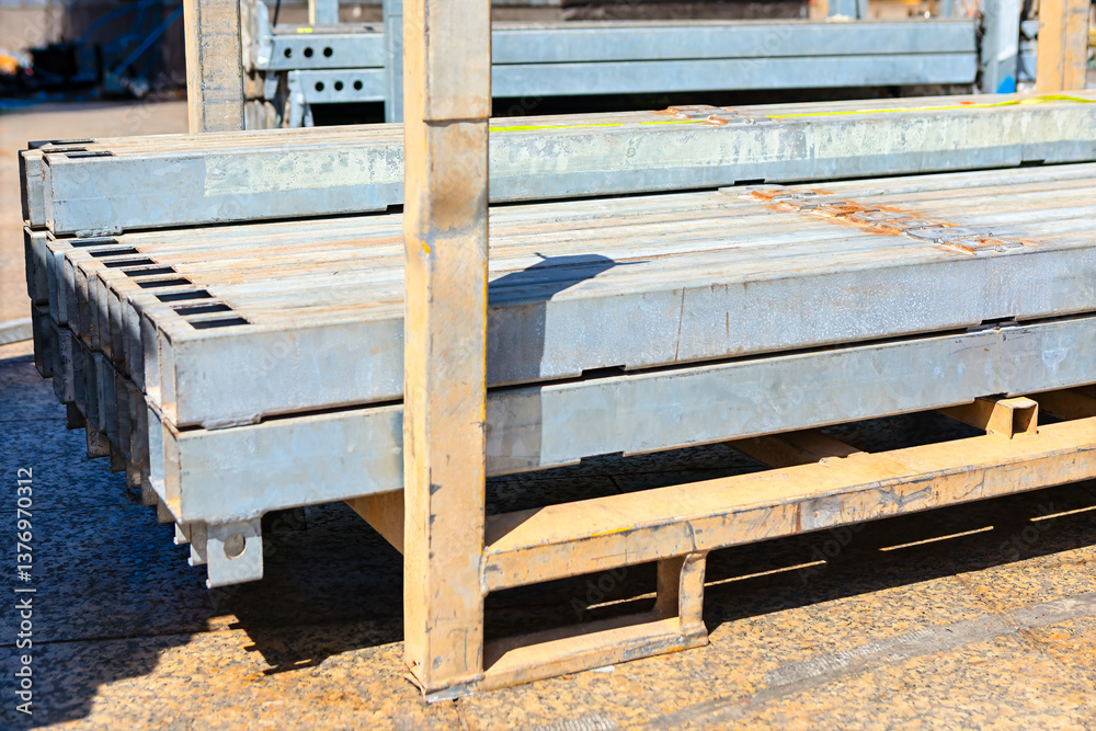 Stack of metal beams, neatly arranged on a metal rack, pallet of industrial and construction setting. Some of beams display rust patches, suggesting they have been exposed to the elements over time