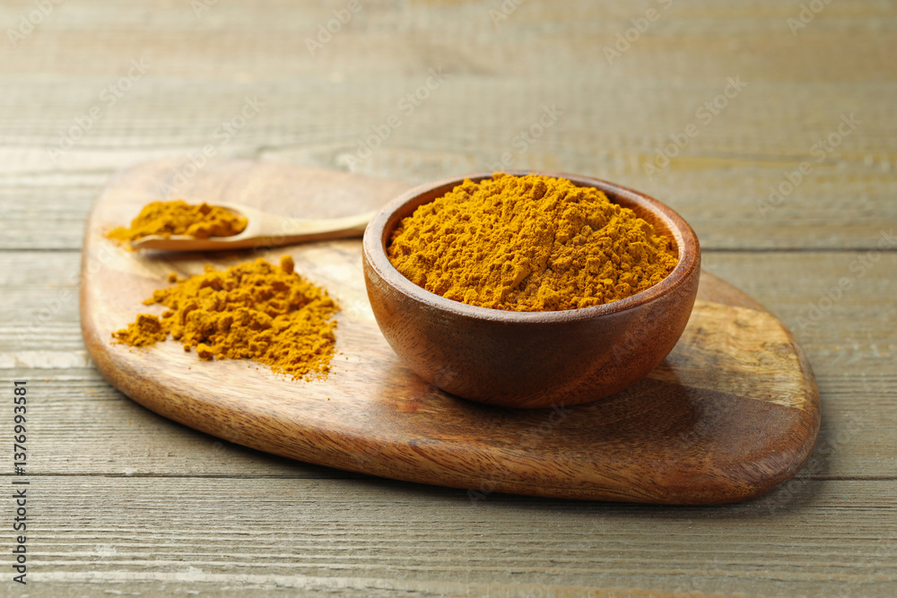 Turmeric powder in bowl and spoon on wooden table, closeup Turmeric powder in bowl and spoon on wooden table, closeup